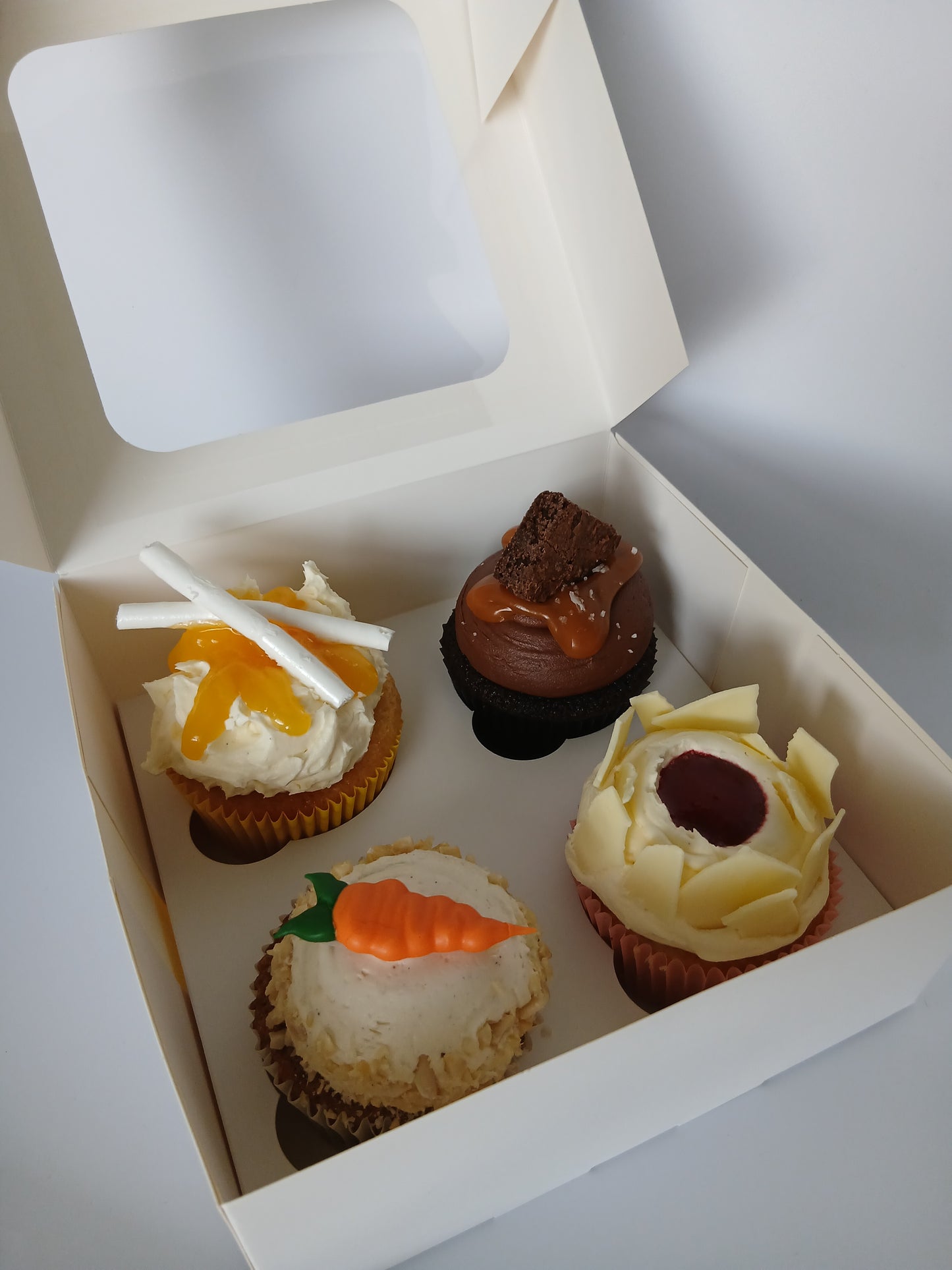 Box of cupcakes with decorative icing on a light background
